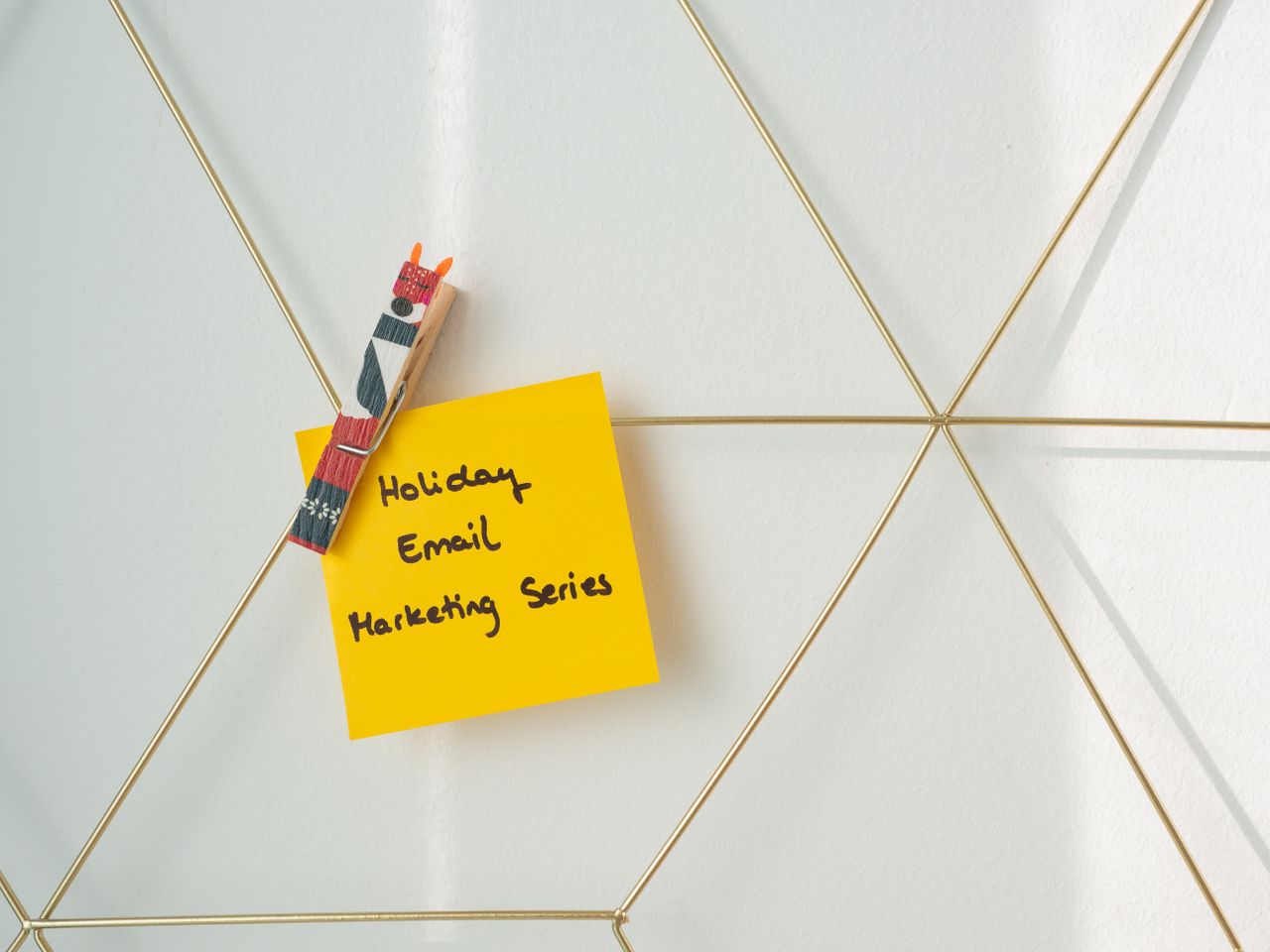 Un post-it jaune vif affichant un message de marketing par email pour les fêtes, fixé sur un mur en structure filaire.